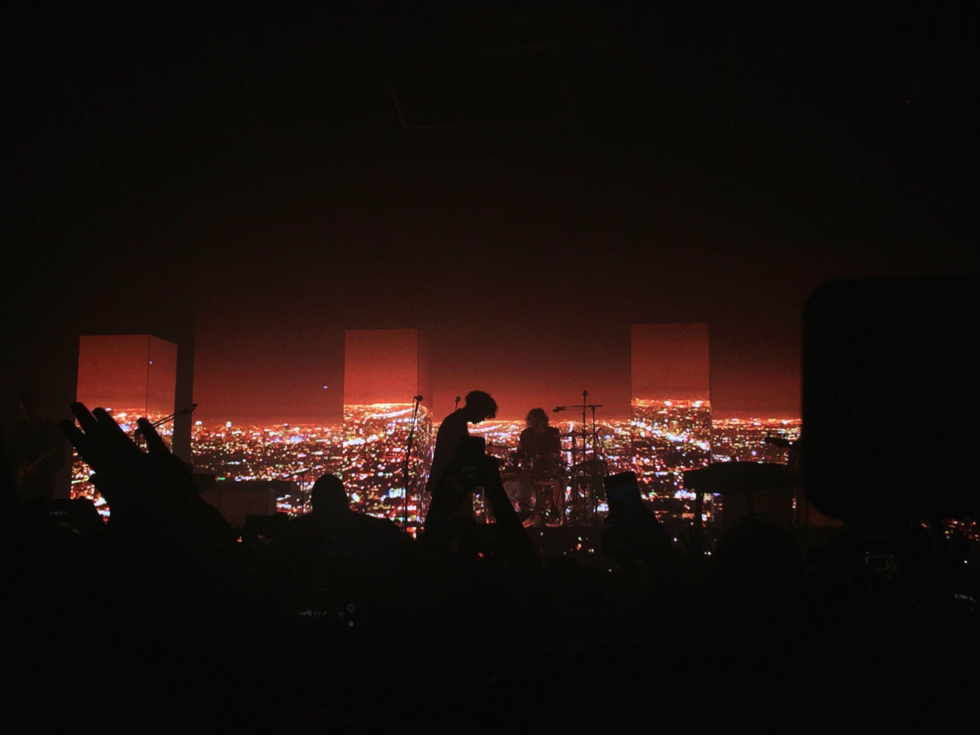Dark concert venue with silhouetted audience and band in front of red cityscape